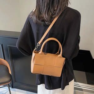 Brown woven leather bucket bag with wide cross-weave texture and adjustable shoulder strap