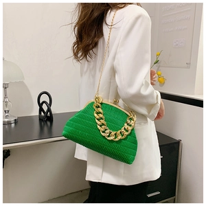 Sac plissé vert avec chaîne dorée épaisse porté par un mannequin en costume blanc