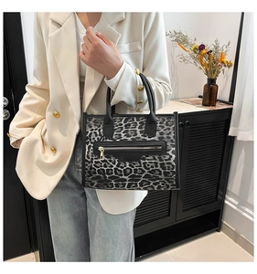 Detail of leopard print tote bag with black leather handles and front zipper pocket