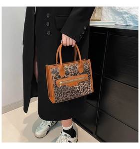 Detail of leopard print tote bag featuring a front zipper pocket and brown leather handles