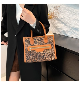 Detail of leopard print tote bag with brown leather handles and golden zipper on dark suit