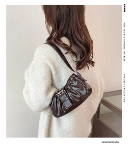 Close-up of a glossy dark brown pleated underarm bag with silver buckle and belt detail