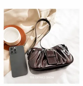 Detail view of glossy pleated chocolate underarm bag with decorative belt buckle and strap