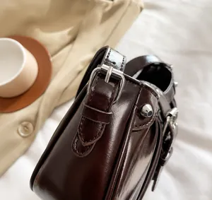 Detail view of dark brown patent leather shoulder bag with polished silver metal buckle