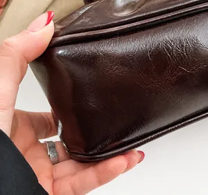 Close-up of precise stitching on deep brown glossy faux leather shoulder bag side