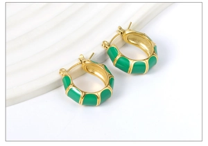 Detail of C-shaped bamboo texture gold and green enamel hoop earrings on ceramic dish