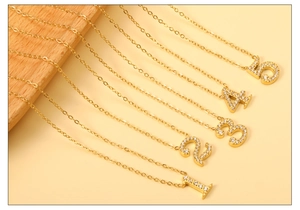 Détail de colliers dorés à l'or 18 carats avec pendentifs chiffres et zircons blancs