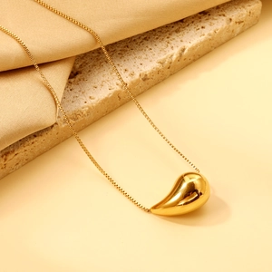 Elegant gold teardrop pendant necklace on marble and silk fabric background