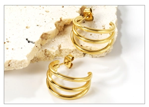 Close-up of triple-layered gold C-shape stud earrings on a textured stone base