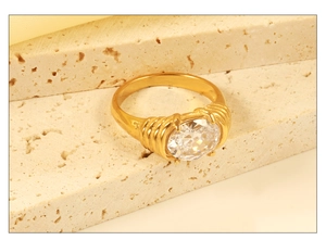 Close-up of gold oval crystal ring with ribbed band on beige textured stone display