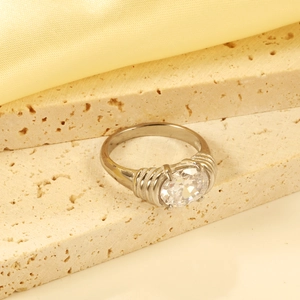 Minimalist stainless steel oval ring with clear gemstone on textured stone and silk