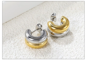 Macro shot of two-tone gold and silver chunky C-shaped metal hoop earrings on stone