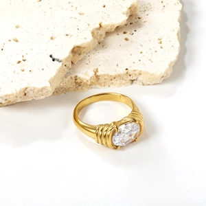 Elegant gold-tone ring featuring oval white gemstone and textured band on stone backdrop