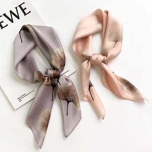 Detail view of two silk scarves featuring realistic ginkgo leaf patterns in grey and pink