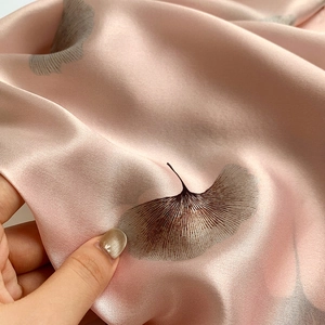 Macro detail of soft pink silk scarf featuring delicate grey ginkgo leaf patterns and luster