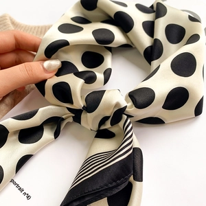 Close-up of silk scarf featuring bold black polka dots and striped edge detail