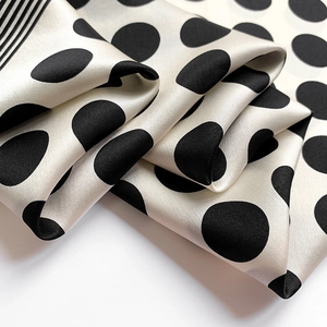 Close-up of silk scarf with large black polka dots and decorative stripes on cream fabric