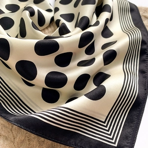 Close-up of silk scarf showing glossy satin texture with black dots and striped border