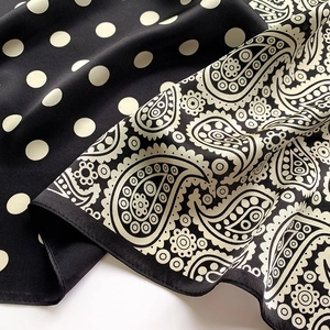 Detailed close-up of silk scarf showing elegant black and white paisley and polka dot patterns