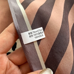 Close-up of 70x70cm mulberry silk scarf label showing 100% silk material and striped texture