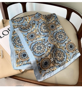 Détail d'un foulard carré en soie à motif mandala bleu posé sur un sac à main beige