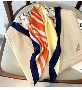 Detail of silk-feel geometric square scarf draped on a beige blazer with a pearl brooch