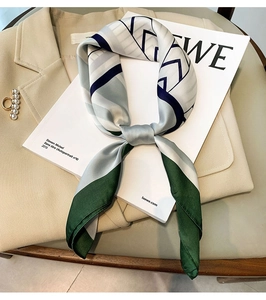 Detailed view of silk-like geometric scarf with green trim and pearl brooch accessory