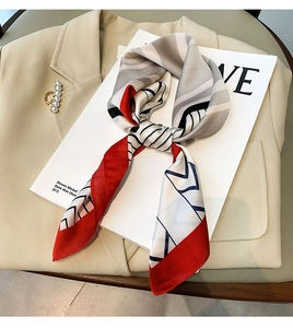 Close-up of geometric silk scarf tied in a bow on a beige blazer with pearl brooch