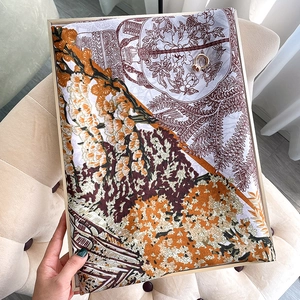 Écharpe en soie à imprimé floral orange et marron disposée sur un canapé beige