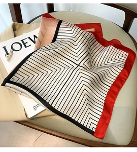 Detail of red and black silk square scarf styled on a blazer with pearl accessories