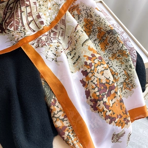 Détail du foulard imprimé feuilles tropicales avec ourlet orange vif et texture de soie