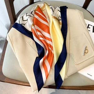 Elegant geometric print silk-like square scarf styled on a beige blazer with pearls