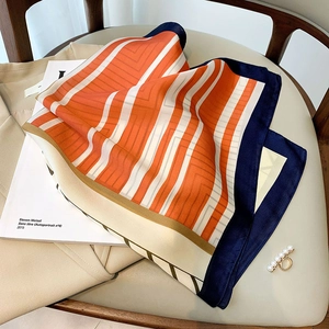 Elegant silk-like square scarf with orange geometric stripes on a stylish leather chair
