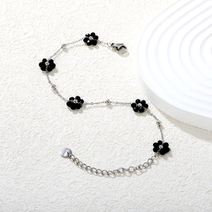 Détail d'un bracelet en acier inoxydable argenté avec cinq breloques fleurs noires et plaque
