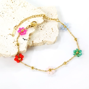 Golden stainless steel floral bracelet with five colorful bead flowers on stone background