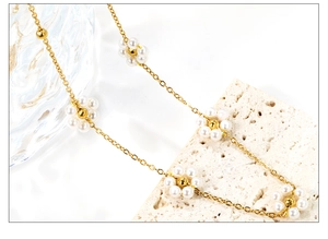 Détail d'un collier en chaîne dorée avec pendentifs marguerites en perles sur fond de pierre