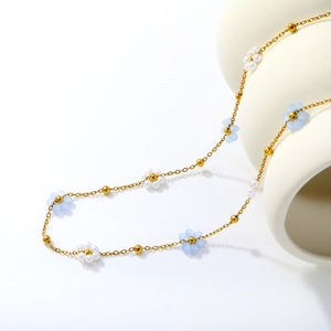 Détail du collier à perles dorées avec fleurs blanches et bleu clair sur céramique