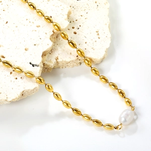 Collier à perles olives dorées avec pendentif perle baroque blanche sur décor de pierre