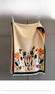 Détail d'une écharpe en jacquard avec motifs floraux, fleurs orange et franges blanches