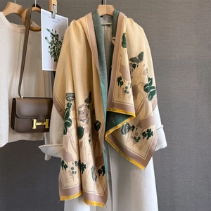 Détail d'une écharpe fleurie vintage avec pompons jaunes sur un long manteau blanc
