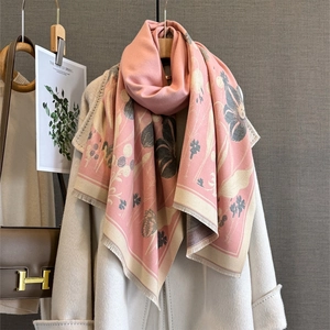 Détail d'une écharpe fleurie rose à franges drapée sur un manteau blanc
