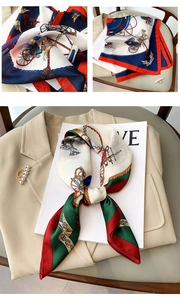 Detail of silk-like neck scarf with chain print and pearl gold buckle on a beige blazer