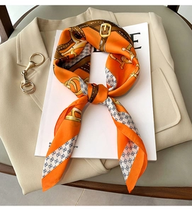 Détail d'un foulard en soie orange à motif de chaîne sur un blazer beige en arrière-plan