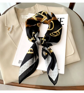 Détail d'un carré de soie avec motifs chaînes et vintage posé sur une veste chic