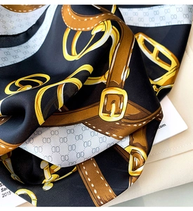 Détail d'un foulard en satin avec motifs de chaînes dorées, ceintures et monogrammes