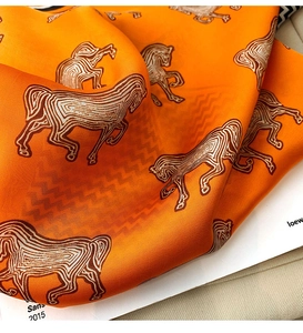 Detailed close-up of orange silk scarf with equestrian horse pattern and satin texture
