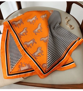 Classic orange silk scarf with horse pattern and herringbone border on leather chair