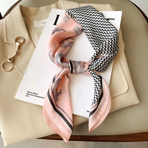 Silk-like fashion scarf with pink horse print and black wave pattern tied on a magazine