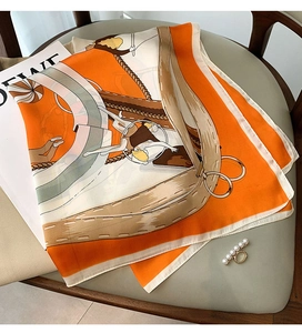 Detail of silk-feel scarf with circus pattern and pearl scarf ring on grey leather chair
