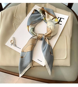 Detail of silk twilly scarf with horse harness print tied on a beige suit jacket